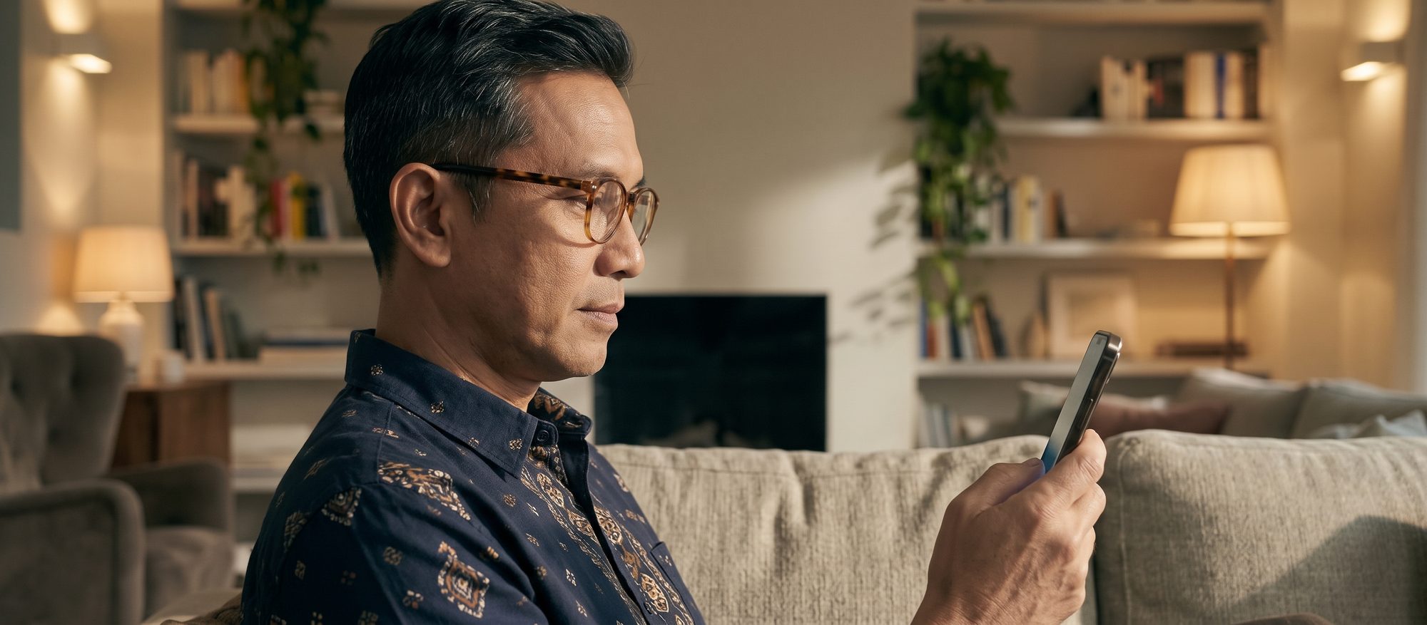 Man in tortoiseshell glasses looking at his phone in a warm living room